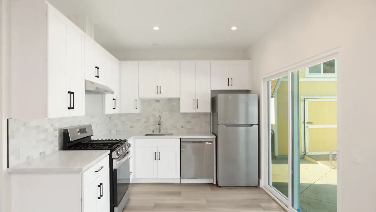 The finished kitchen of the Brea garage conversion: white shaker cabinets, a marble-look backsplash, stainless appliances and a slider to the yard