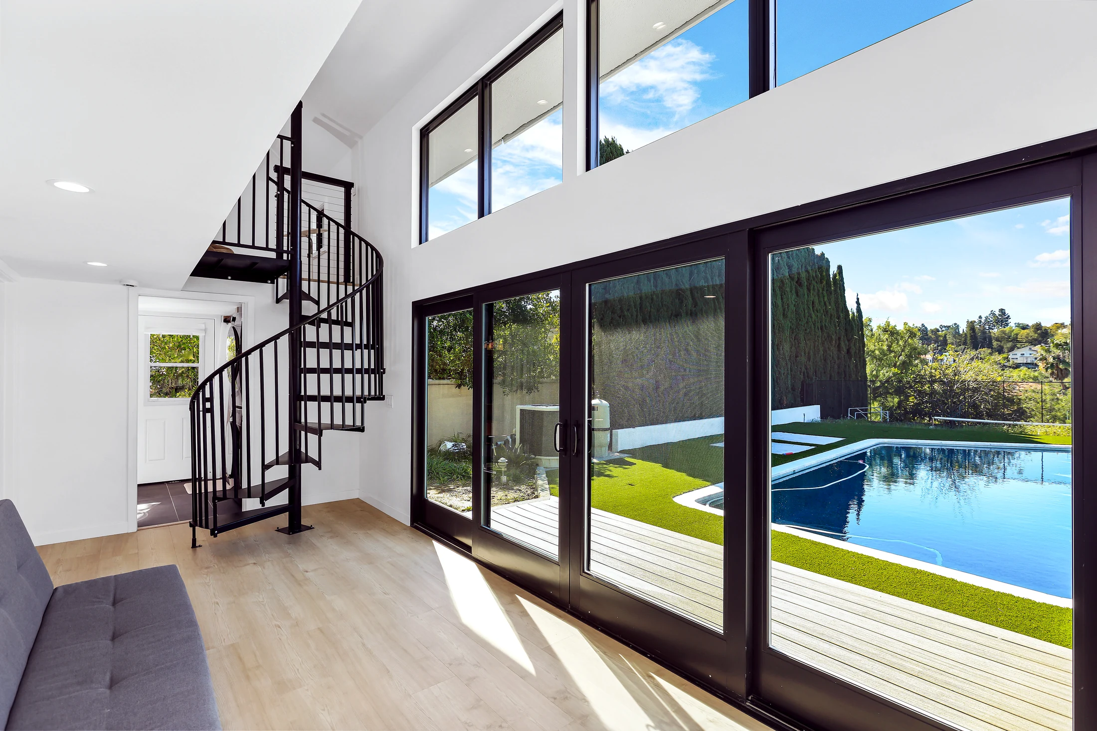 A double-height room with floor-to-ceiling glass onto a pool and yard, in a modern Avorino build in Orange County