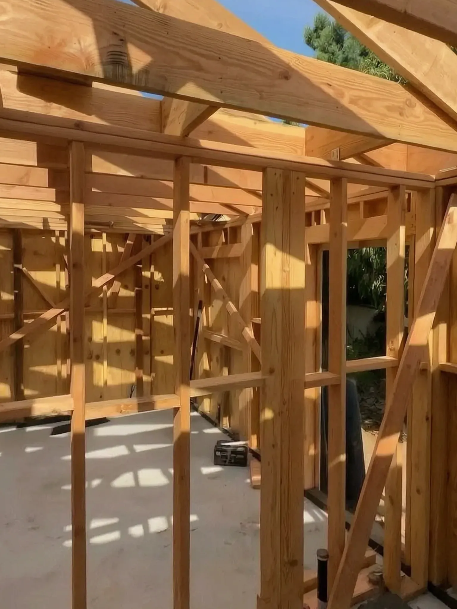 Attached ADU under construction — wall framing and roof rafters against the sky, Orange, Avorino
